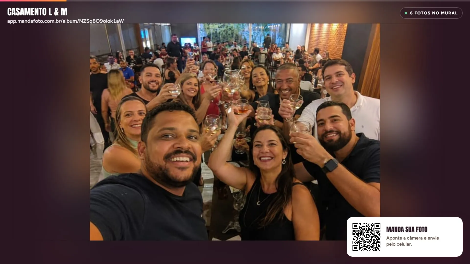 Mural ao vivo do MandaFoto numa TV: selfie de convidados brindando, o nome do álbum no topo e o QR Code para enviar fotos no canto